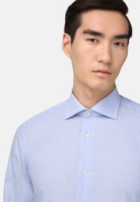 Světle modrá, pruhovaná košile s knoflíky a klasickým límečkem, se dvěma knoflíky u krku. Bavlněný materiál, jemná textura.