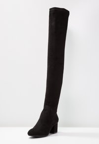 Botas negras sobre la rodilla hechas de suave tejido de ante, con un tacón cuadrado y un diseño de punta redondeada y lisa. Sin herrajes ni patrones visibles.