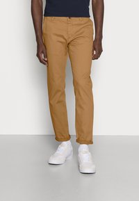 Kaki chinos med rak passform, tillverkade av bomull, med knappstängning och upprullade ärmar, parat med vita sneakers och strumpor.