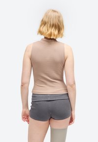 Person with short blonde hair wearing a sleeveless beige top, gray shorts, and a beige compression sleeve on the left leg, facing away.