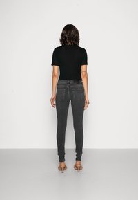 Camiseta preta ajustada combinada com jeans cinza justos. Os jeans possuem bolsos traseiros e uma textura suave e elástica. O modelo usa sandálias de salto em tom de areia.