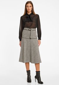 Schwarze durchsichtige Bluse mit Halsbanddetail, kombiniert mit einem knielangen grauen Rock mit Gürtel und dezentem Muster, abgerundet mit schwarzen Ankle Boots.
