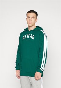 Grön hoodie med vitt "ADIDAS"-logotyp, snörning i huva och sidosträck. Har en framficka och ribbade ärmslut. Mjukt material.