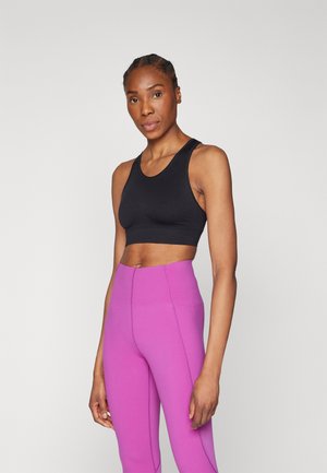 Zwarte crop top met een ronde halslijn en racerback ontwerp, gecombineerd met hoge, naadloze, felroze leggings. Zachte textuur.