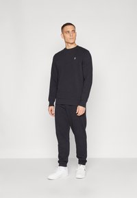 Czarnoszary sweatshirt i dopasowane dresy; materiał z mieszanki bawełny, ściągacze na rękawach; mały emblemat na piersi; w zestawie z białymi sneakersami.