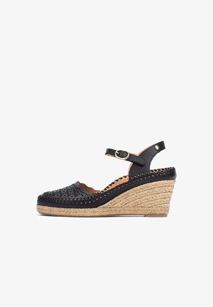 Sandale compensée en cuir noir avec design ajouré, talon recouvert de jute, sangle réglable et surface texturée.