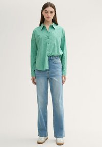 Camisa de botones verde claro con lunares texturizados, combinada con vaqueros de tiro alto de color azul claro y zapatillas blancas. Look simple y casual.