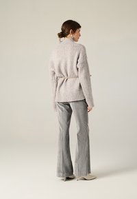 Maglione grigio chiaro con texture e vita con cinturino, abbinato a pantaloni a campana grigi a righe e scarpe con tacco beige, visto di spalle.