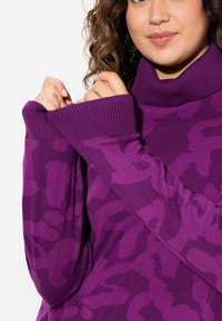 Pull violet avec un col montant et des poignets côtelés larges, présentant un motif texturé de léopard dans des nuances plus sombres de violet.