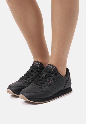 Zapatos deportivos negros hechos de cuero sintético, con puntera redonda, cierre de cordones en la parte frontal y una suela de goma texturizada con un acento marrón.