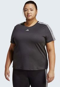 Black athletic t-shirt with white three-stripe design on shoulders, round neckline, short sleeves, and loose fit, worn with black leggings.