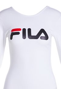 Maglietta bianca a maniche lunghe realizzata in tessuto liscio, con un grande logo FILA nero e rosso sul petto. Collo rotondo classico.