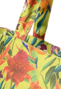 Floral handtas in felgeel, met ingewikkelde rode en paarse bloemen, groene bladeren, textiel en stevige hengsels.