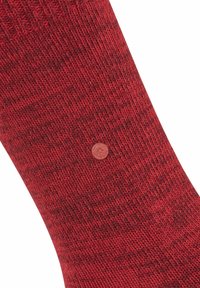 Calzino rosso con texture, caratterizzato da un motivo lavorato a maglia, con un piccolo logo circolare come dettaglio. Il tessuto sembra caldo e accogliente.