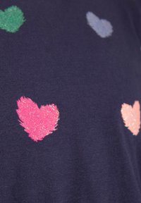 Laivaston t-paita, jossa on useita kirkkaan värisiä, kimaltavia sydäntarroja vaaleanpunaisena, vihreänä ja vaaleansinisenä teksturoidulla kankaalla.