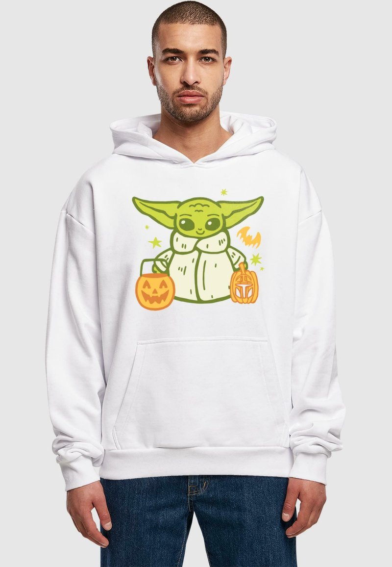 Witte hoodie met een cartoonfiguur met groene huid en grote oren, die twee oranje pompoenvormige snoepemmer vasthoudt; relaxte pasvorm, voorvak.