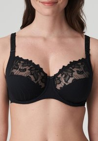 Mustat pitsiliivit, joissa on läpinäkyvät yläpaneelit, kukkapitsiyksityiskohtia ja tekstuuriset alaosat. Säädettävät hihnat ja kiinnitys keskellä.