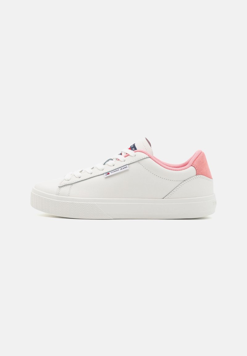 Baskets blanches avec des accents en suède rose au talon, semelle en caoutchouc texturée et lacets plats. Comprend une petite étiquette logo sur le côté.