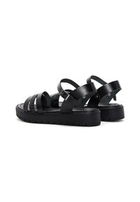 Sandales en cuir noir avec plusieurs lanières, un détail tressé et une semelle épaisse noire. Présentent une boucle réglable et un semelle texturée.