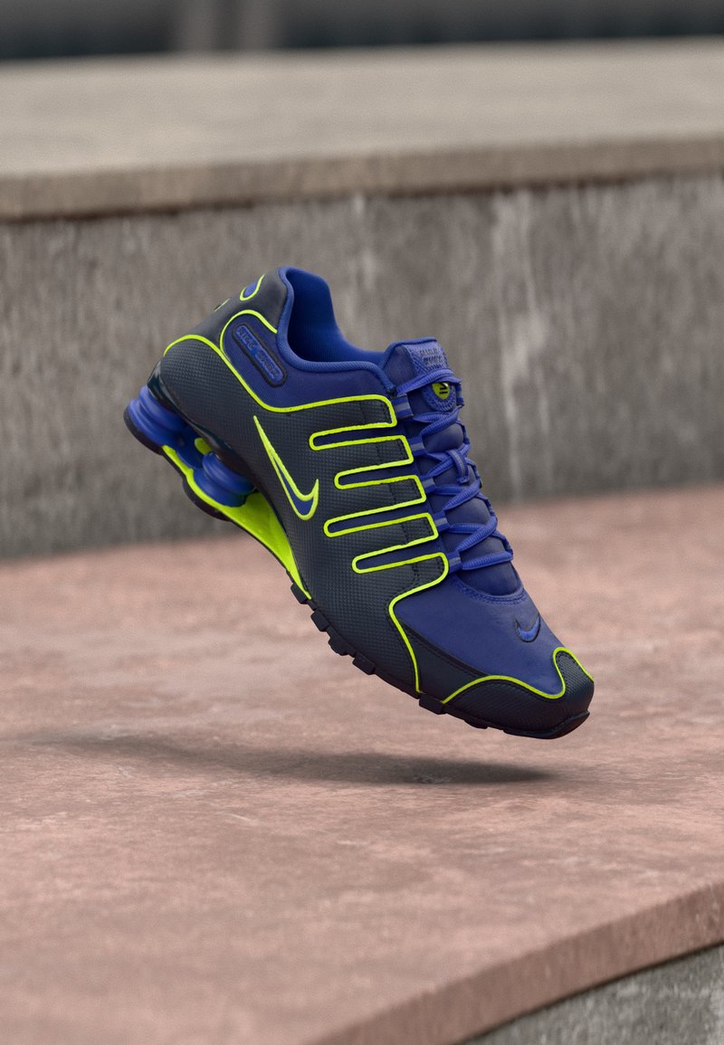 Μπλε και νέον πράσινο αθλητικό παπούτσι Nike με ορατές ελατήρια στη φτέρνα, τοποθετημένο στον αέρα πάνω από σκάλες από σκυρόδεμα.