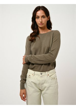 Olijfgroene gebreide trui met een ronde halslijn en ribgebreide manchetten, gecombineerd met lichtbeige high-waisted jeans. Soepel textuur met minimale details.