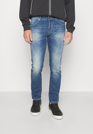 Jasnoniebieskie dżinsy o slim fit, z wyblakłym wykończeniem, pięcioma kieszeniami i subtelnymi detalami whiskering. Noszone z czarnymi trampkami.