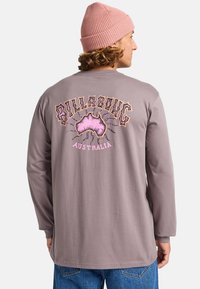 Szara koszula z długim rękawem z kolorową grafiką "Billabong Australia" oraz wzorem mapy Australii z tyłu. Wełniana czapka dodaje faktury.