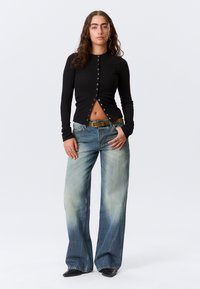 Haut noir à manches longues avec boutonnières et coupe courte, associé à un jean évasé délavé clair avec un effet dégradé et une ceinture.