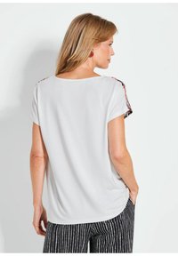 Witte top met korte mouwen en een relaxte pasvorm, met een patroontextuur langs de schoudernaad, gecombineerd met zwart-witte broeken met patroon.