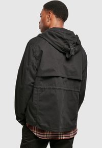 Black hooded jacket with a relaxed fit, featuring a front pocket, a layered back design, and adjustable cuffs. Textured fabric, casual style.