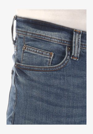 Jean en denim avec un lavage bleu foncé, design à cinq poches, couture visible et finition texturée avec un petit détail de poche arrière.