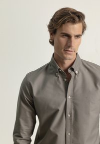 Camisa gris de botones, hecha de una tela suave, con mangas largas, botones en contraste y un pequeño detalle de logo en el pecho.