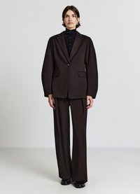 Blazer marrone scuro su misura con un bottone singolo e due tasche, abbinato a pantaloni a gamba larga coordinati, indossato sopra un dolcevita nero.