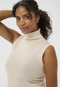 Heledbeez turtleneck ilma varrukatooted, mis on valmistatud pehmest, sädelevalt kummist kangast. Omab keha lähedalt sobivat siluetti ja soonikdetailide vaheldust kaelas.