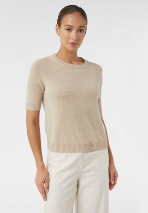 Beige knitted short-sleeve sweater with a round neckline and ribbed cuffs and hem. Soft texture and relaxed fit, paired with light-colored pants.