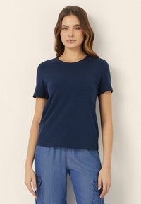 Tricou bleumarin cu mânecă scurtă, confecționat dintr-un material moale, cu gât rotund, croială lejeră și textură netedă. Asortat cu pantaloni din denim.