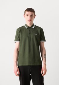 Grønn polo skjorte med ribbet krage som har hvite detaljer, knappestolpe og brodert logo på brystet. Korte ermer, strukturert stoff.
