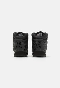 Sneaker alte nere con upper in pelle e rete testurizzata, caratterizzate da un audace design con ritagli sul tallone e una suola in gomma spessa.