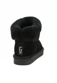 Schwarzer Wildleder-Überknöchelstiefel mit einem plüschigen Fellkragen. Verfügt über eine schwarze Gummisohle mit strukturiertem Rand und einem Logo-Patch an der Ferse.