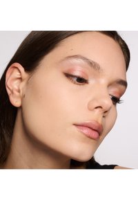 Primer plano del rostro de una mujer que muestra piel suave, maquillaje ligero con tonos rosados en los párpados y labios naturales. Pelo oscuro parcialmente visible.