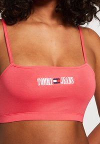 Korallfarbener Crop-Top aus elastischer Baumwolle, mit schmalen Trägern und einem weißen, gestickten "TOMMY JEANS"-Logo auf der Vorderseite.