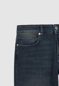 Jeans de mezclilla azul oscuro con una textura suave, diseño estándar de cinco bolsillos y cierre de botón de metal. Desgaste mínimo cerca de la cinturilla.