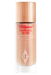 Bottiglia in vetro con base conica, liquido rosa chiaro, tappo in rosa dorato testurizzato e testo rosso con la scritta "Hollywood Flawless Filter."
