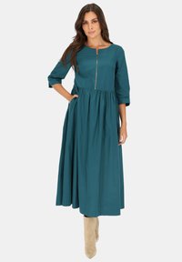 Turkusowa sukienka midi z rękawami trzy-czwarte, marszczonym pasem i zamkiem błyskawicznym z przodu. Miękka tkanina z delikatnym połyskiem i bocznymi kieszeniami.