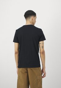 Tricou din bumbac negru cu mânecă scurtă și guler rotund, prezentat din spate. Are o textură netedă și nu sunt vizibile logo-uri sau modele.