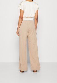 Světlebéžové široké kalhoty z jemné tkaniny s elastickým pasem, v kombinaci s těsným, slonovinovým topem s krátkým rukávem. Hladký povrch a uvolněný střih.