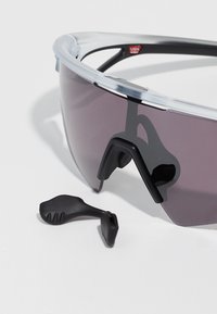 Skjold-stil sports solbriller med mørkt tonede linser og løse sorte justerbare næsepuder på en hvid overflade.