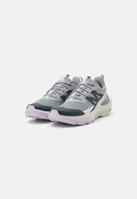 Une paire de chaussures de course grises et noires avec des semelles violet clair et des semelles intermédiaires blanches, positionnées côte à côte sur un fond blanc.