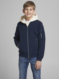 Námořnická modrá bunda s bílou kapucí, na zip a boční kapsou. Nosená přes bílou košili a v kombinaci s modrými džíny. Rovný, hladký povrch.