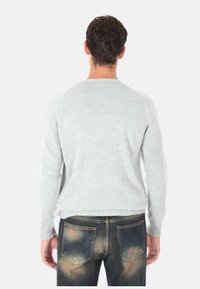 Maglione grigio chiaro in maglia con scollatura rotonda e polsini a coste. Il retro presenta una texture liscia e un design semplice e lineare. Indossato con jeans scuri.